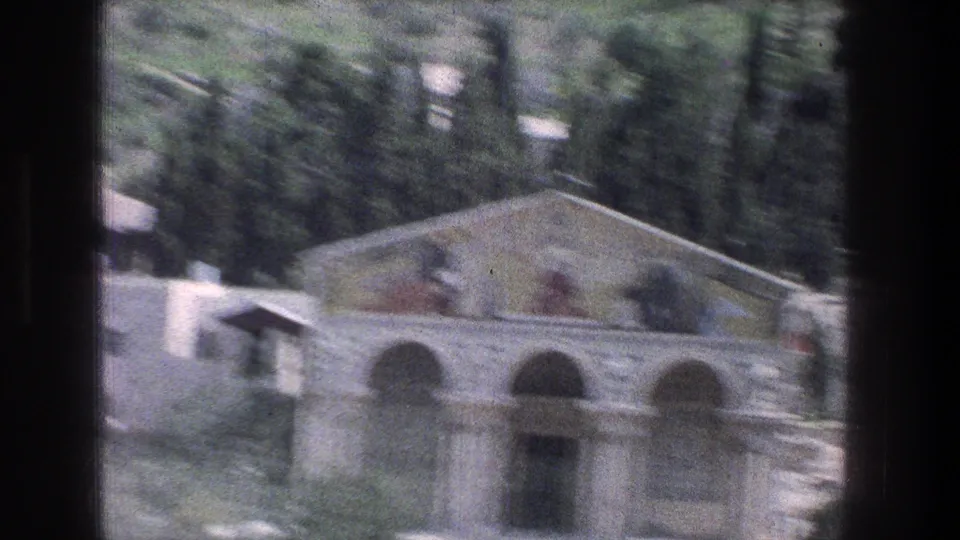 1976 Jerusalem home-movie frame with motion blur on an ornate arched building, hillside greenery, and dark vehicle-window borders.