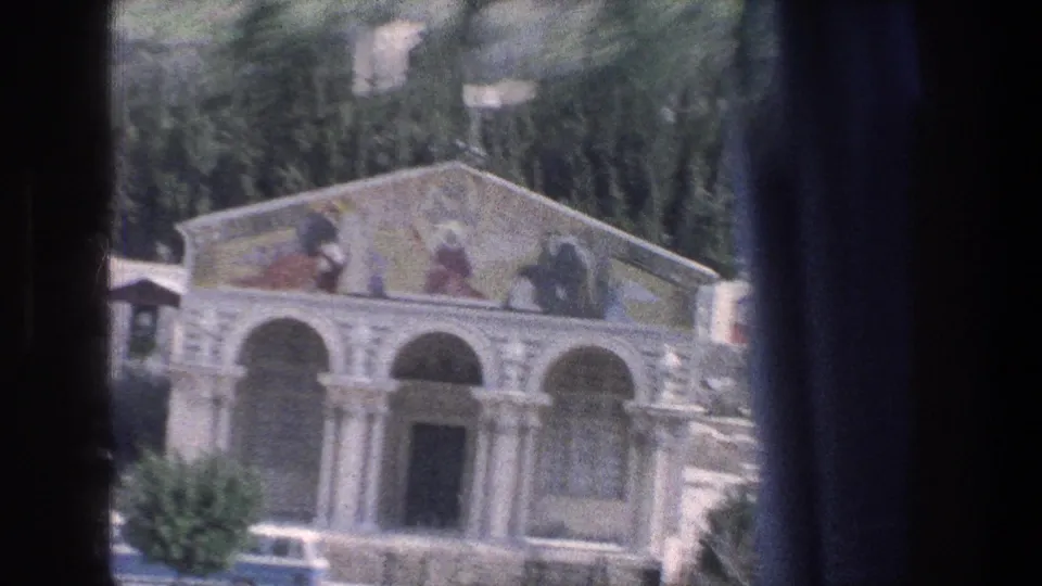 1976 8mm Jerusalem frame showing a closer roadside view of an ornate arched facade with columns, painted pediment, and nearby trees.