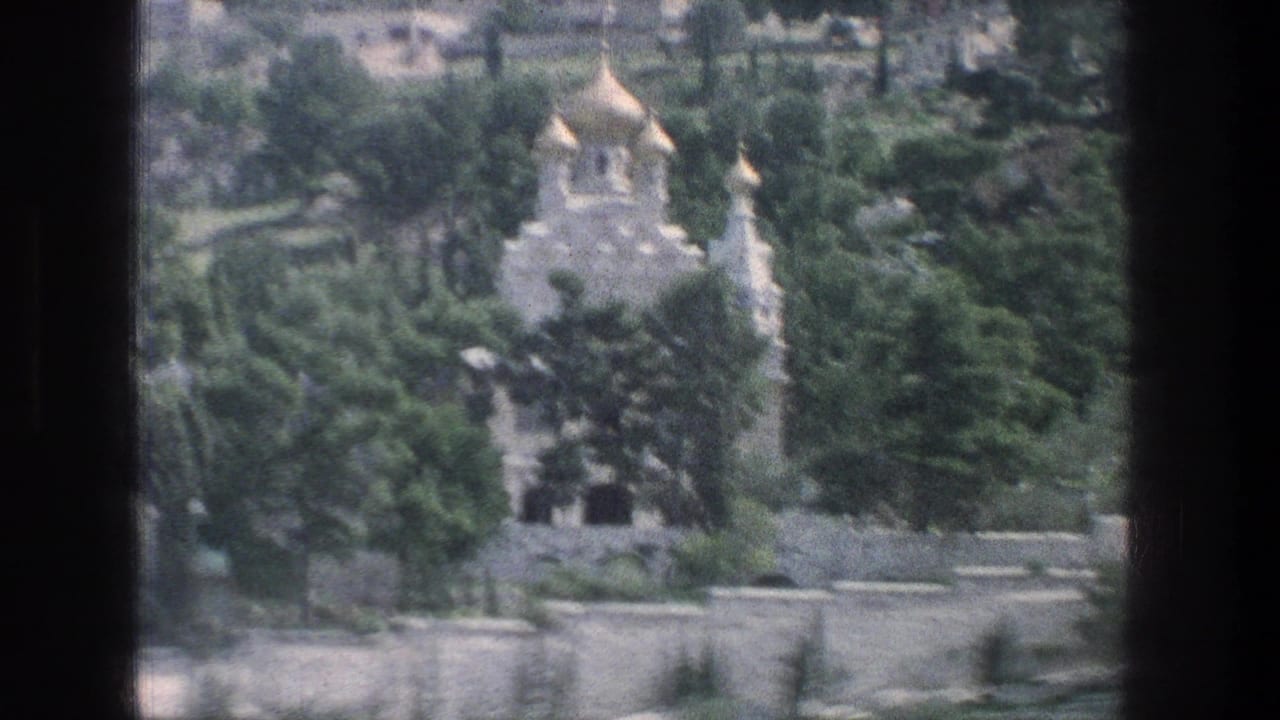 1976 Jerusalem 8mm frame showing a distant pale stone church with golden onion domes behind dense trees and terraced stone walls.