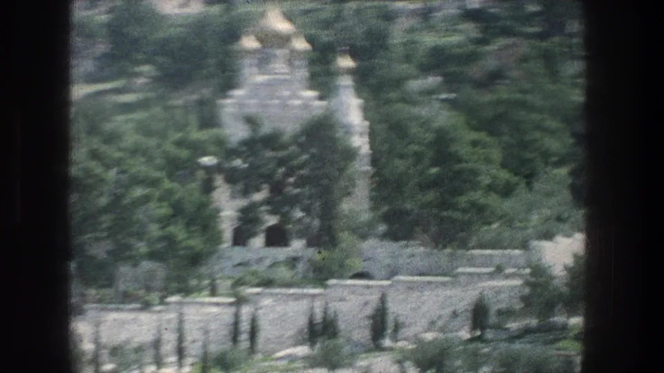 1976 Jerusalem 8mm frame showing a distant white stone religious building with gold domes set among greenery and stone walls.