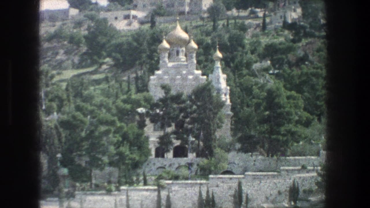 Gold-domed white building surrounded by trees and stone walls in a hillside view.