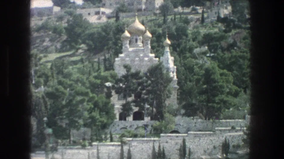 1976 Jerusalem view of a white stone landmark with gold domes, arched openings, trees, and surrounding stone walls.
