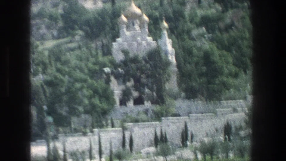Soft 1976 Jerusalem frame showing a gold-domed white stone building partly obscured by trees and motion blur.