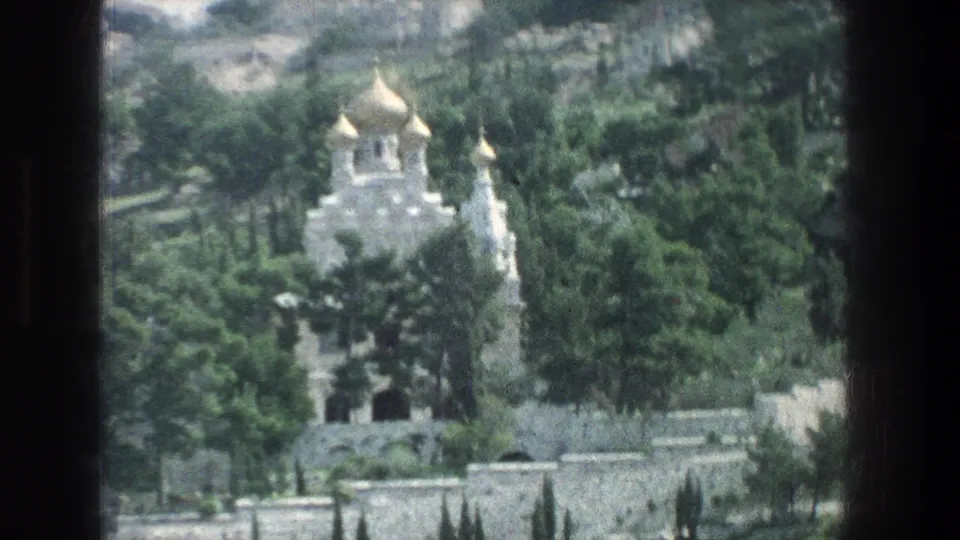 1976 Jerusalem footage shows a golden-domed hillside building partly obscured by trees and viewed from a moving vehicle.