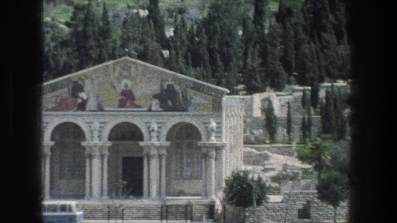 1976 Jerusalem exterior showing a white stone arched building with faded murals in the pediment, hillside trees, stone walls, and a dark central doorway.