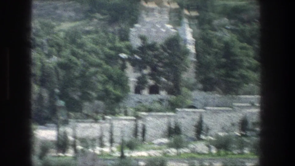 1976 Jerusalem home-movie frame with blurred trees, stone retaining walls, pale paths, and hillside landscaping as the camera continues its pan.