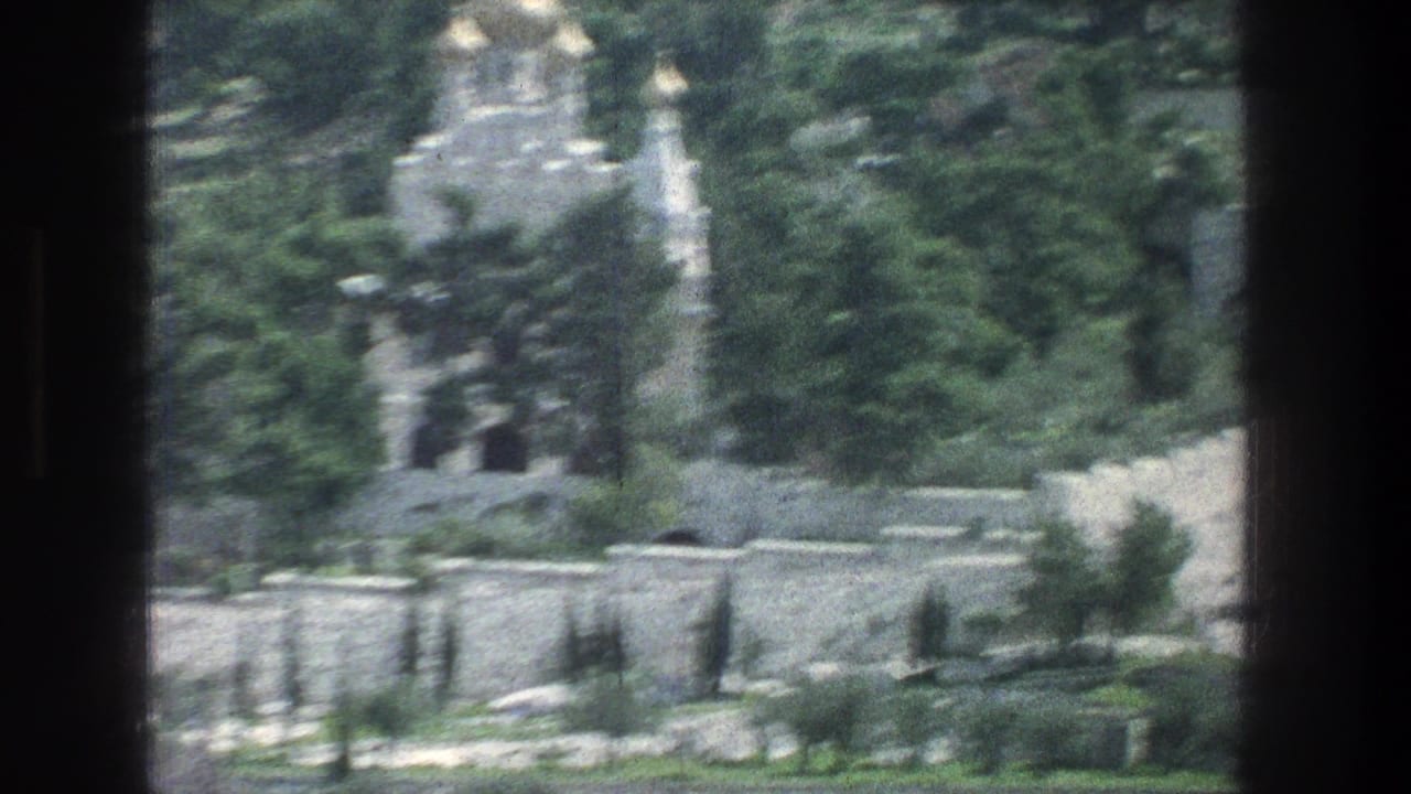 Distant stone tomb partly obscured by dark vertical window frames and trees.