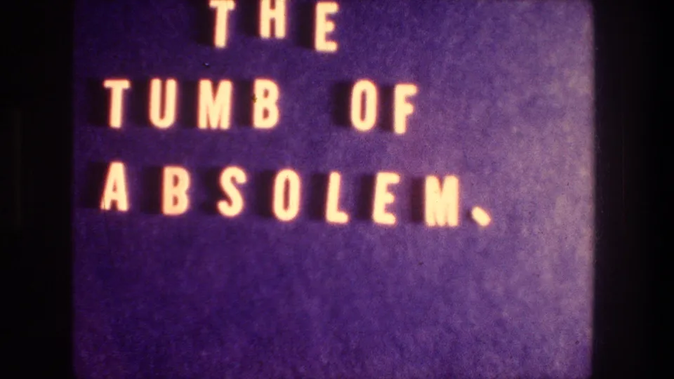 Filmed 8mm title card in purple tones with the handwritten-style text "THE TUMB OF ABSOLEM."