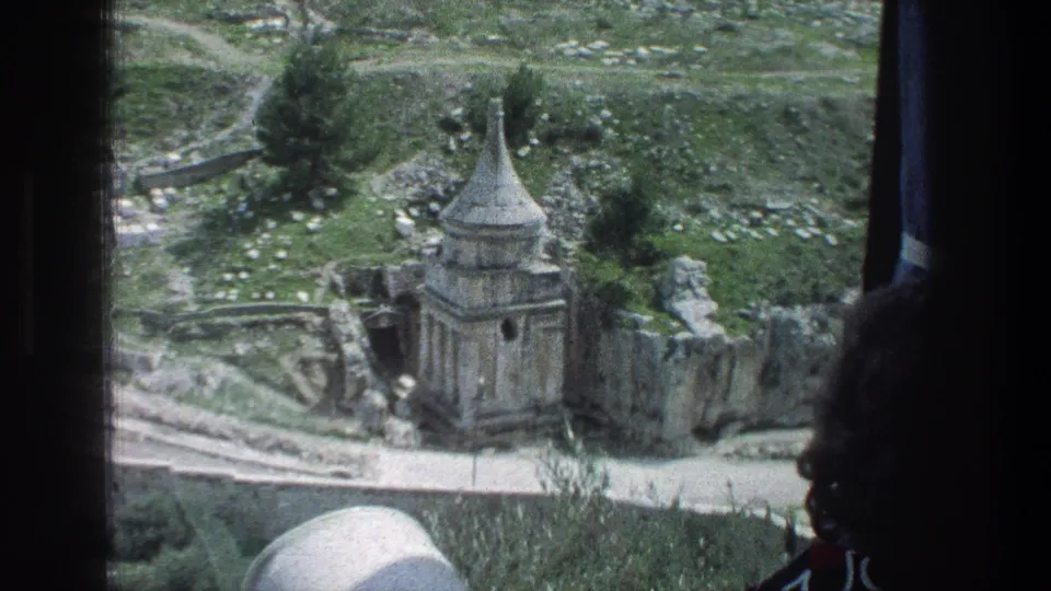 Jerusalem landmark view of the Tomb of Absalom with green grass, paths, trees, and dark framing from a window or vehicle interior.