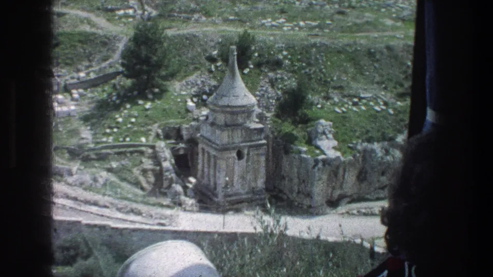 1976 Jerusalem travel footage shows a stone ruin with a conical roof viewed from inside a vehicle, with grassy slopes beyond.