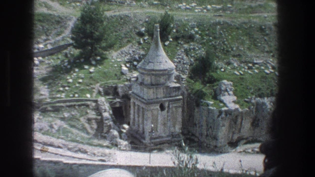 1976 8mm Jerusalem view of a conical-roofed stone structure surrounded by rocky ruin walls and patches of greenery.