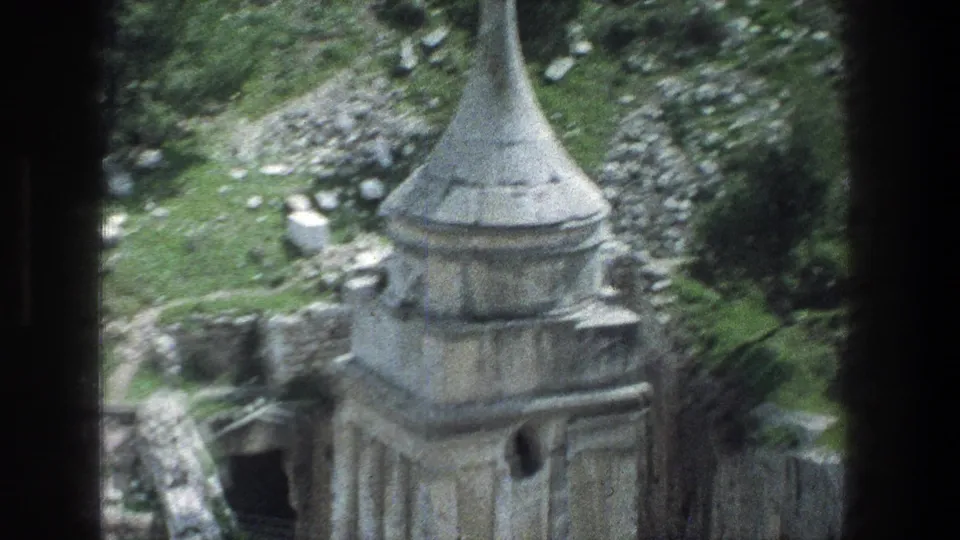 1976 Jerusalem home-movie frame with a closer, slightly blurred view of the conical stone roof, masonry base, dark opening, and rocky ground.