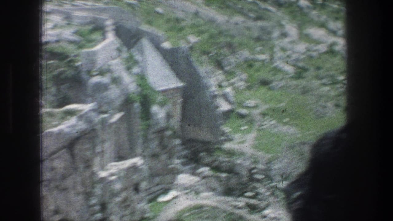 1976 8mm Jerusalem view of gray rock, green patches, and stone ruins seen from a shaded opening or overlook.