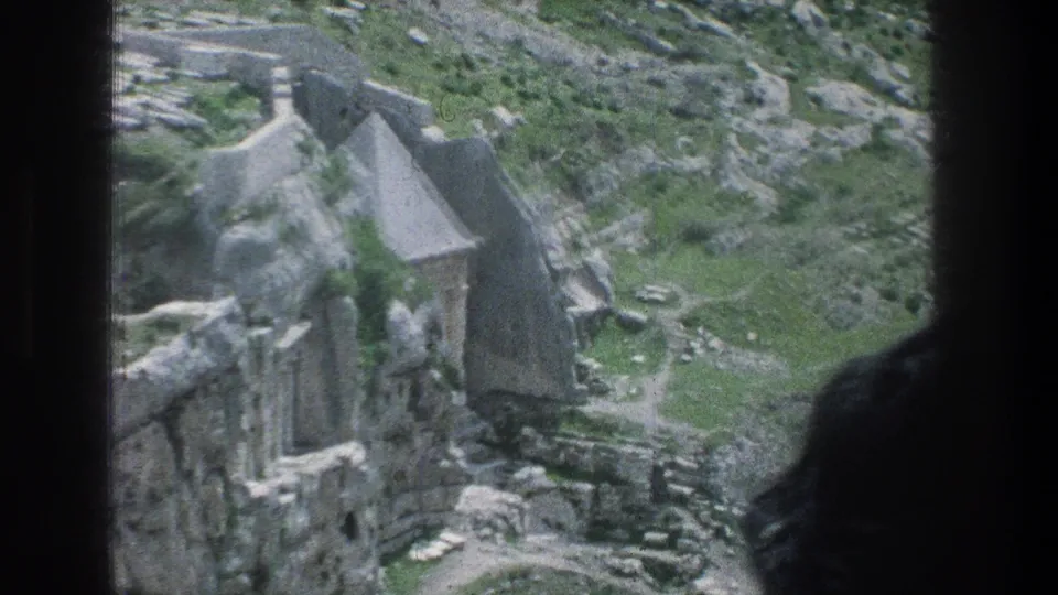 1976 8mm Jerusalem frame showing pale stone ruins, rough rock, grass, and a dark window or doorway edge.