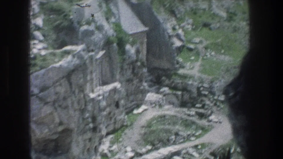 1976 8mm Jerusalem footage showing weathered stone ruins, a winding path, rocky ground, and sparse greenery from an elevated viewpoint.