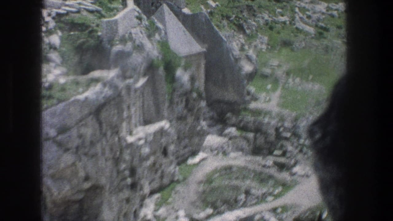 1976 Jerusalem home-movie frame with ruins, a small roofed stone structure, rocky terrain, and vegetation seen through dark foreground edges.