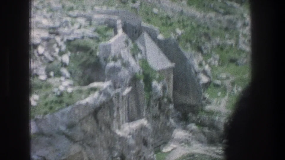 1976 8mm aerial view over Jerusalem stone ruins, with low walls, rough terraces, and green ground visible through soft film grain.