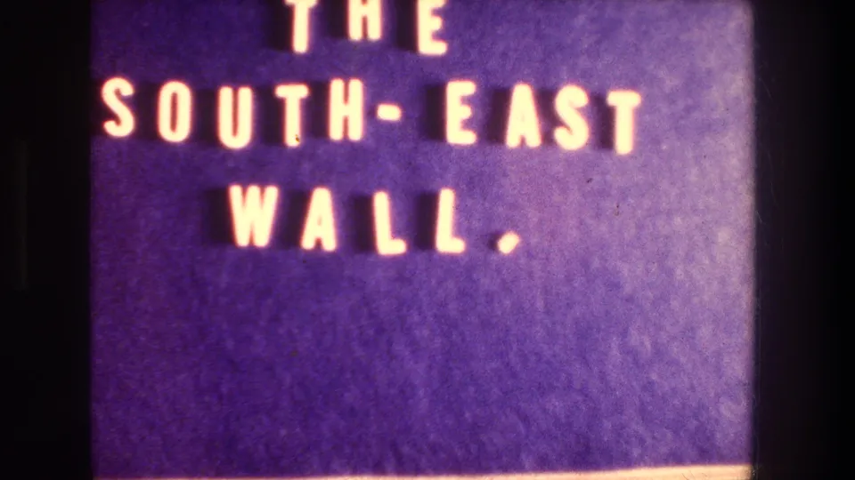 8mm title card reading THE SOUTH-EAST WALL in pale lettering on a purple background, confirming the subject named in the reel.