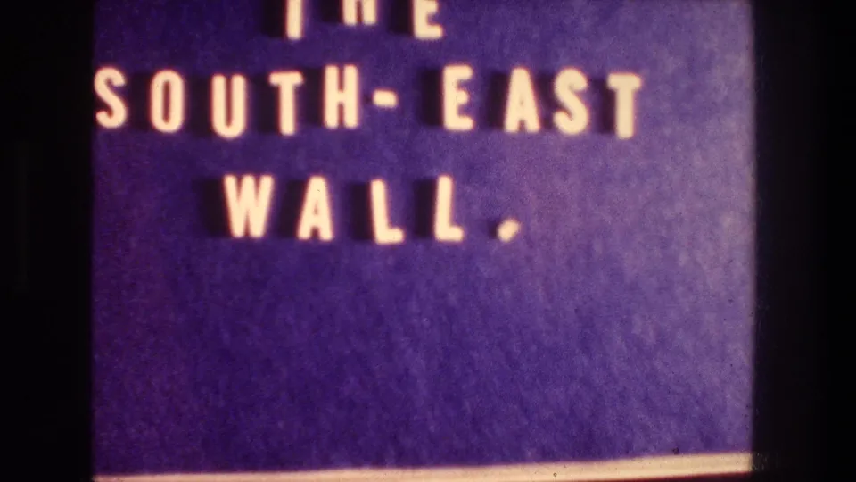 Visitor-shot 8mm view of the South-East Wall sign, with yellow text on a deep purple background.
