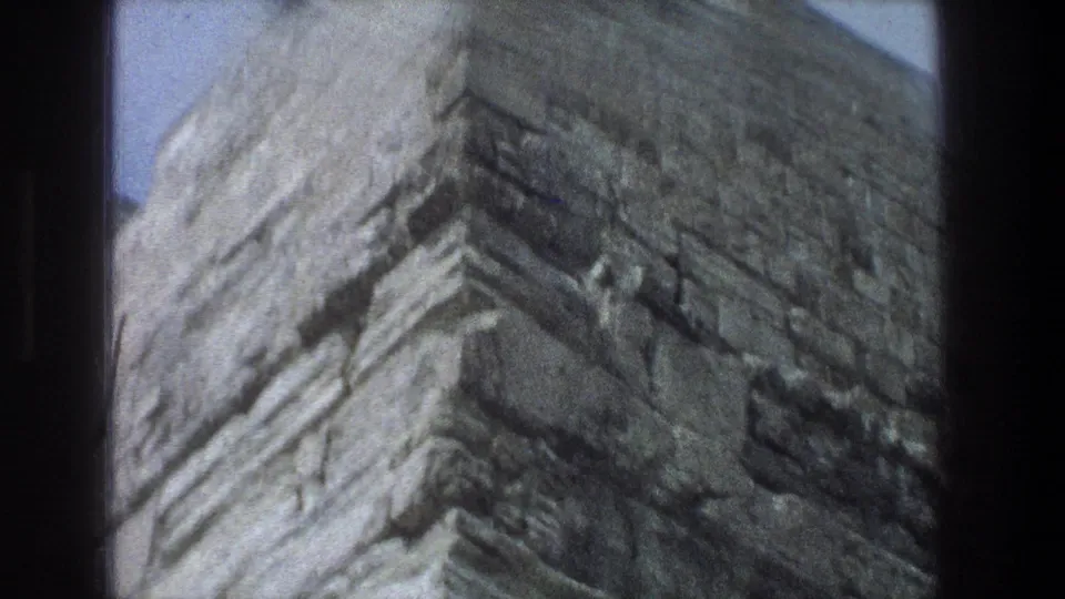 1976 Jerusalem 8mm frame showing a rough, weathered stone wall rising beneath a clear blue sky.