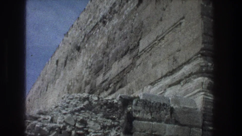 1976 Jerusalem 8mm frame showing an angled stone wall face with rubble or low masonry near the base.