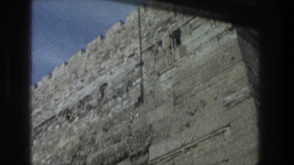 1976 8mm Jerusalem frame with the camera angled up along rough stone courses toward the crenellated top of a large wall.