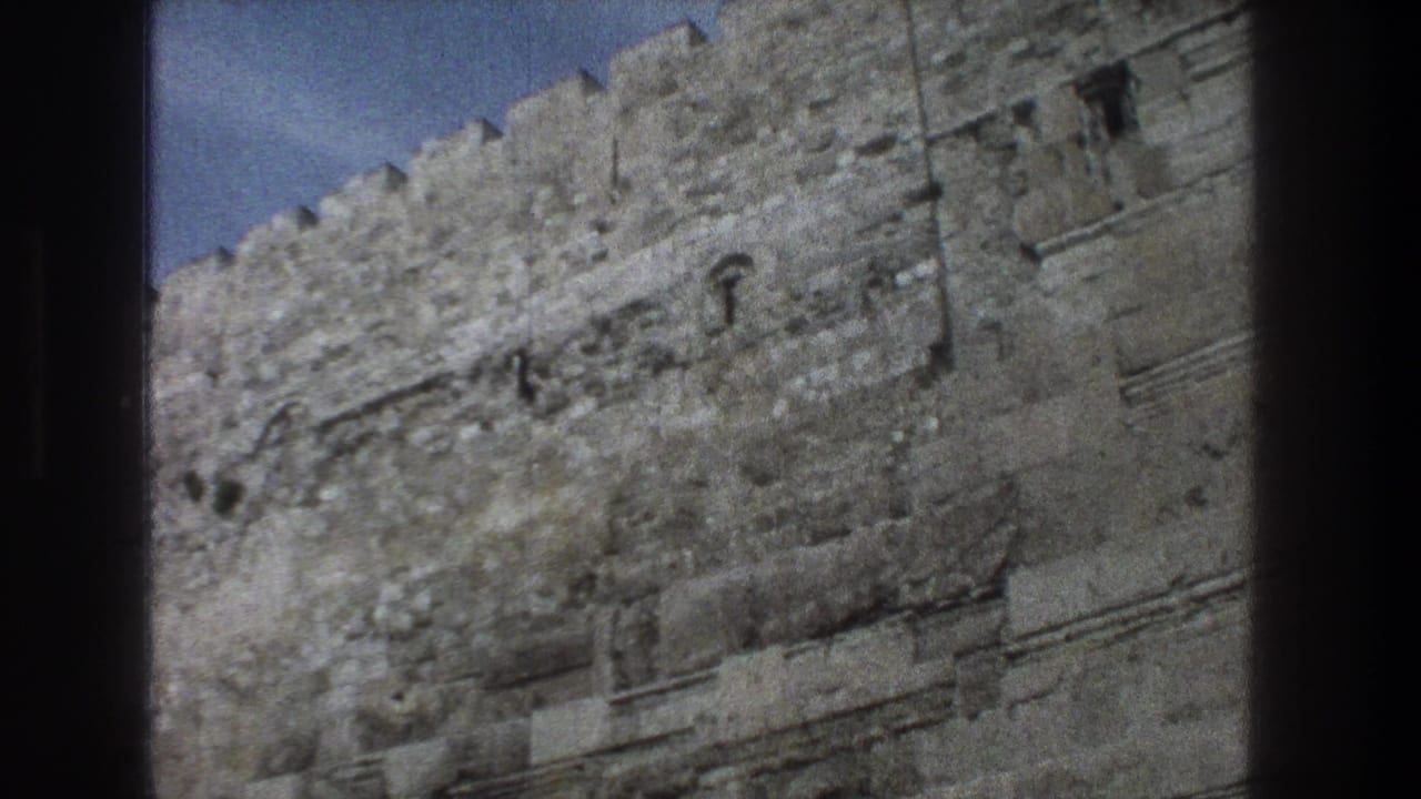 Crenellated stone wall with small openings under a blue sky.