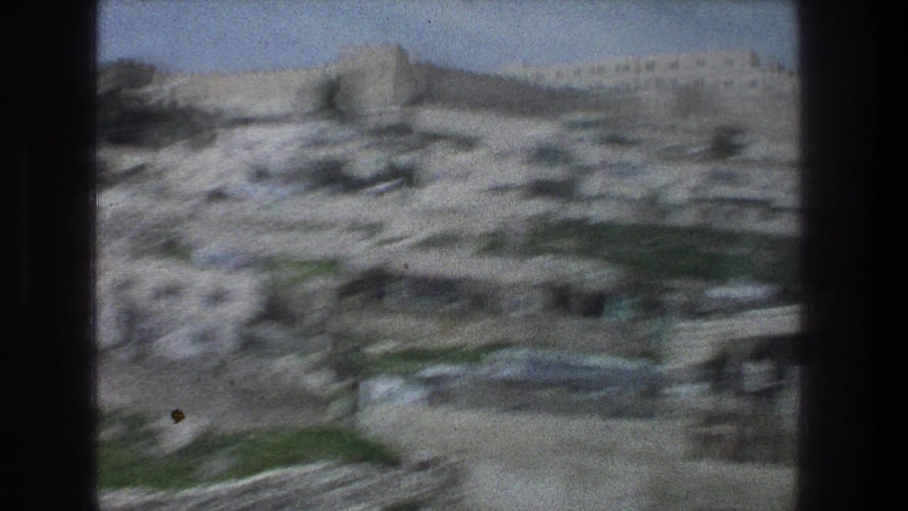 1976 Jerusalem home-movie frame with blurred stone hillside structures, pale walls, and sky during a moving pan.