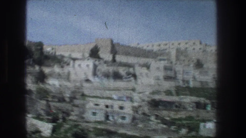 Jerusalem 8mm frame from 1976 with pale stone buildings, terraced ground, dark trees, and distant hillside walls.