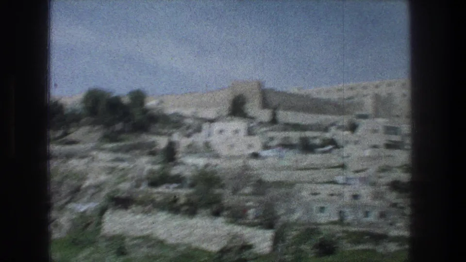 1976 Jerusalem 8mm frame showing a soft, distant view of stone village buildings and hillside terrain.