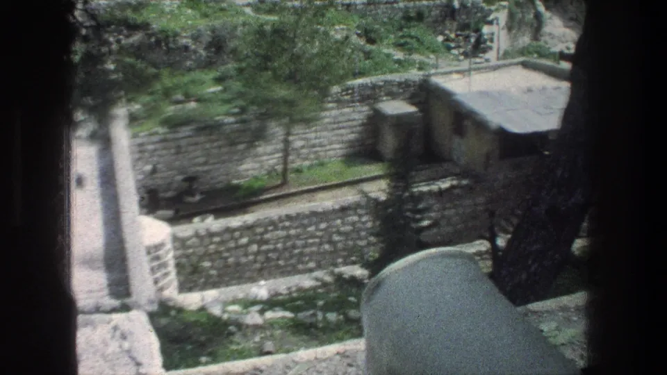 Elevated 1976 Jerusalem view of stone retaining walls, a narrow path, trees, and a small flat-roof building.