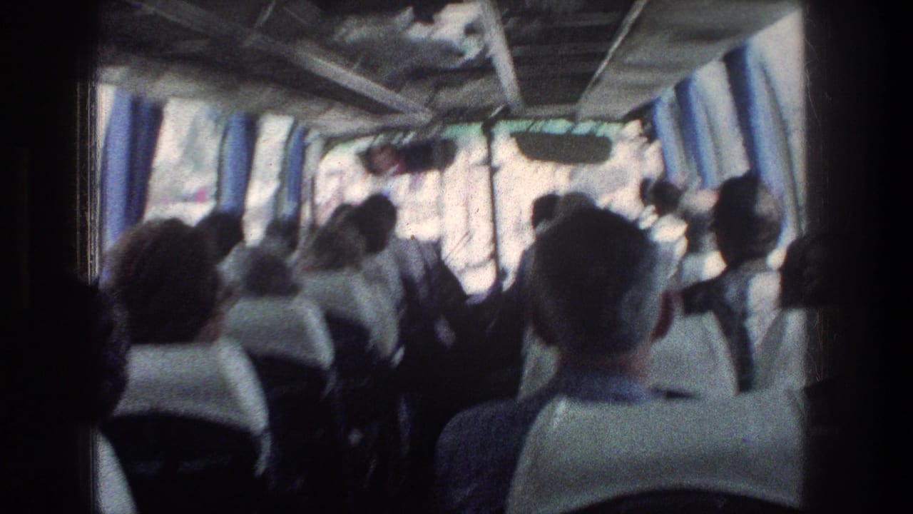 Blurred view of seated bus passengers with bright windows and blue curtains along the side.