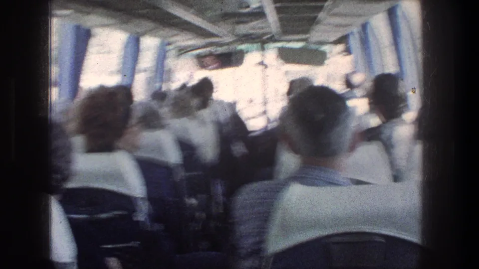 Handheld 8mm frame from inside a Jerusalem bus in 1976, showing adult passengers and rows of seats during a rough ride.