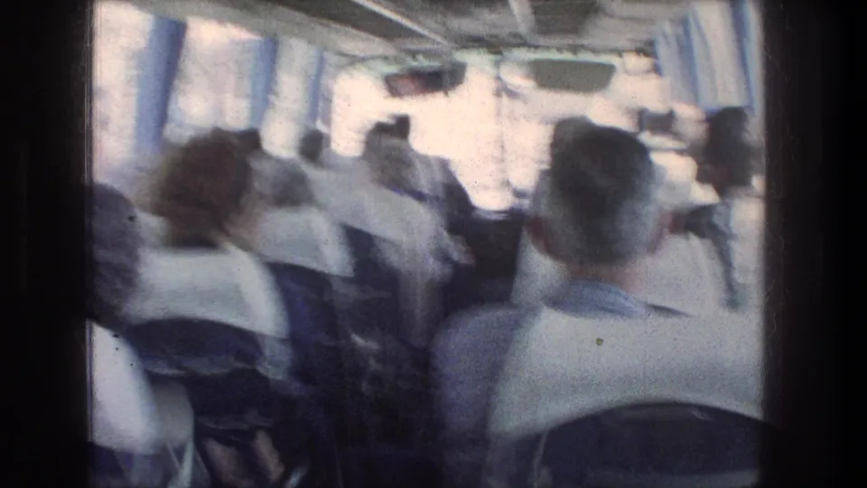 Soft 8mm frame from the Jerusalem bus ride, with seated passengers and blue curtains visible during motion.