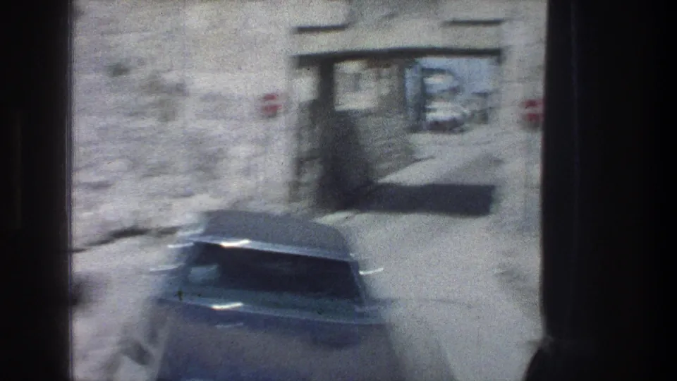 Jerusalem street view from the moving bus, showing a dark vintage car beside a stone wall and archway.