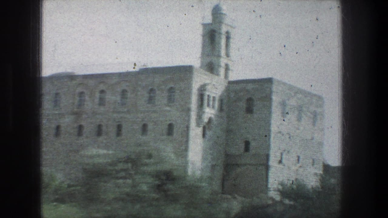 1976 Jerusalem travel footage frame with a large stone structure, arched windows, and tower seen from a moving vehicle.