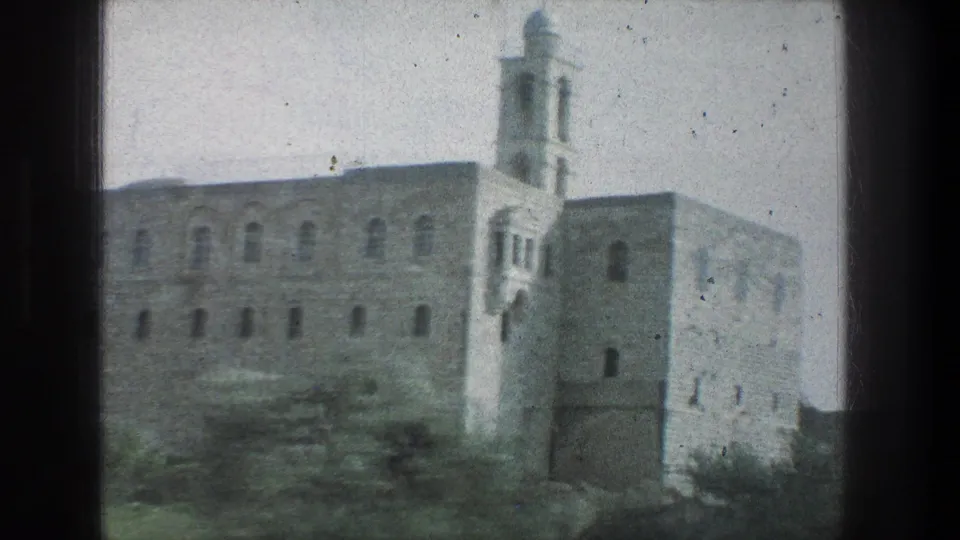 1976 Jerusalem travel footage frame with a large stone structure, arched windows, and tower seen from a moving vehicle.