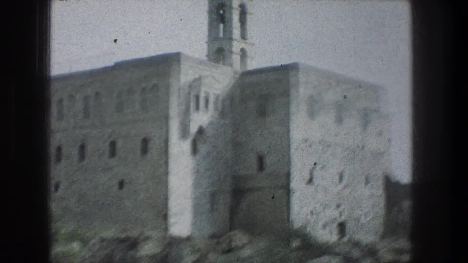 1976 Jerusalem 8mm frame showing a closer drive-by angle on a stone building corner, tower, and arched entry.