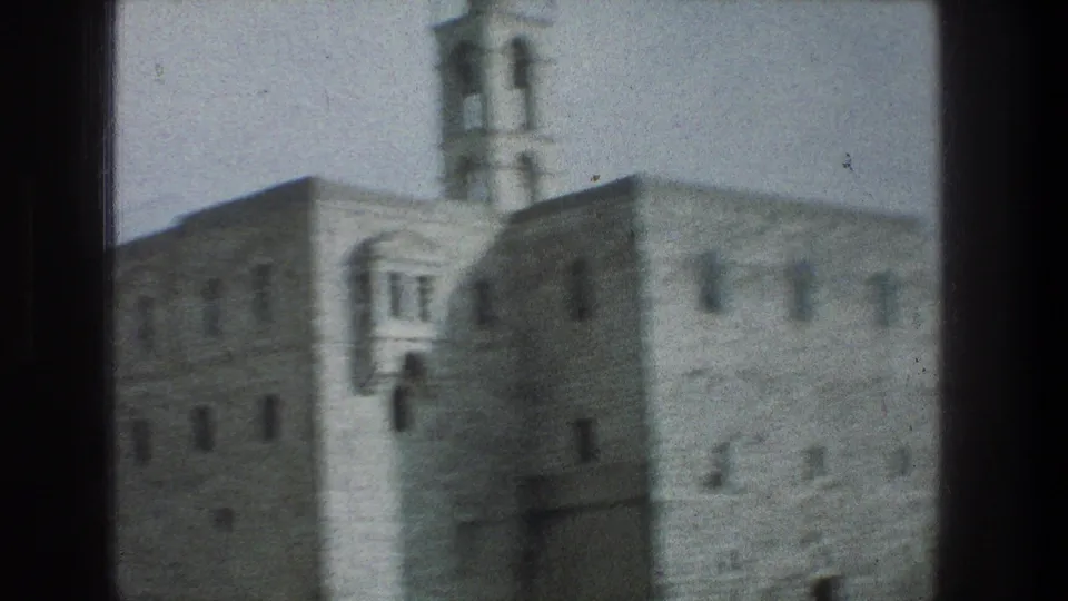 1976 Jerusalem home-movie frame with stone walls, a tower, and small windows seen in soft focus from a vehicle.