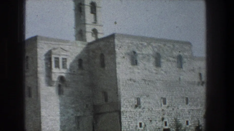 1976 8mm Jerusalem footage showing a pale stone building with arched windows and a bell tower framed by a dark window edge.