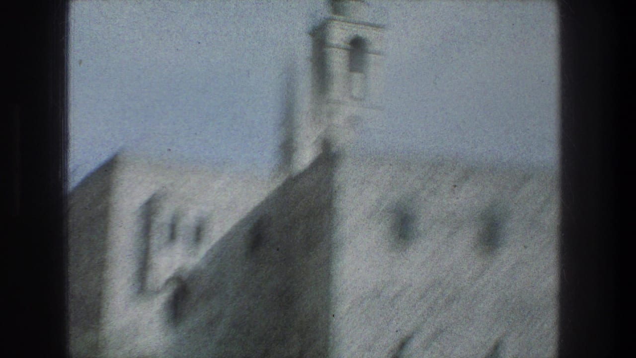 Soft 1970s 8mm view of a Jerusalem stone structure and bell tower, partially obscured by a dark window divider.