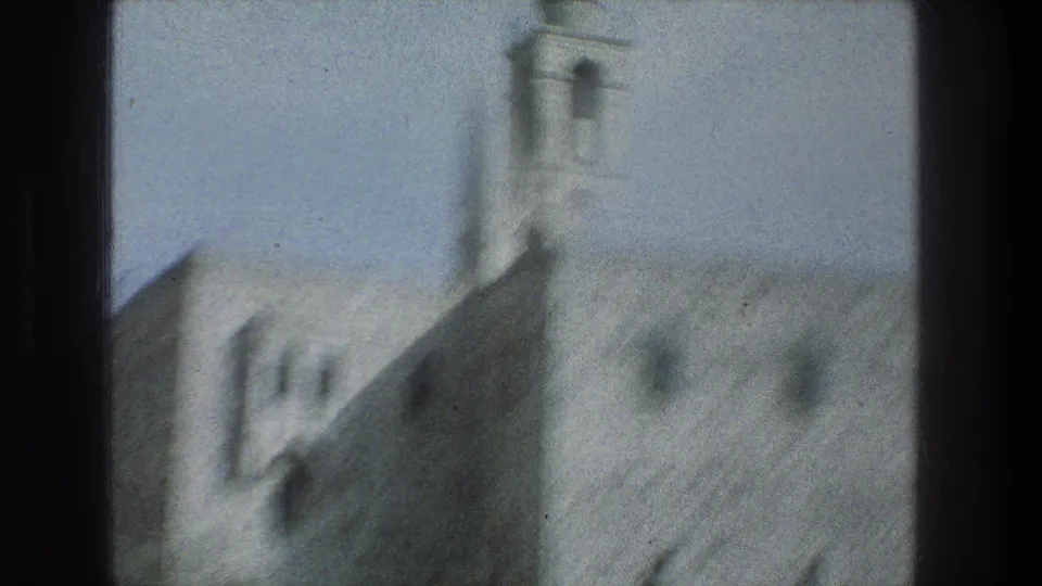 Soft 1970s 8mm view of a Jerusalem stone structure and bell tower, partially obscured by a dark window divider.