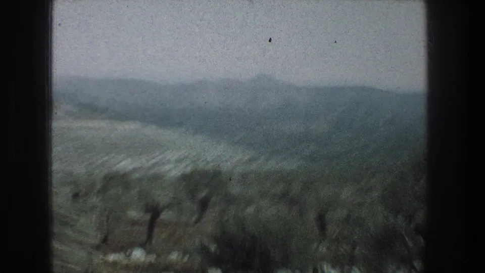 1976 Jerusalem travel footage looking past a dark window frame toward soft hills and scrubby open land.