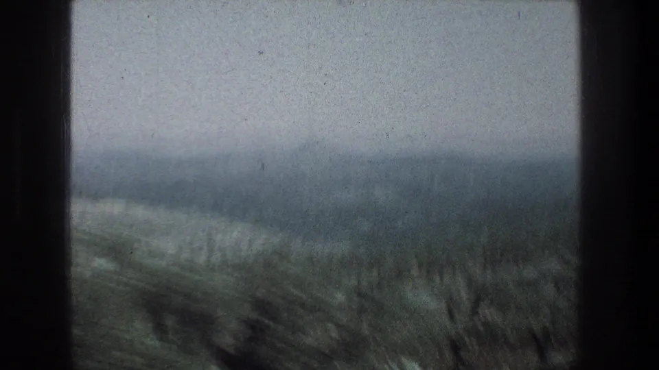 A muted 8mm view of hills and rough foreground land near Jerusalem, framed by dark window or vehicle edges.
