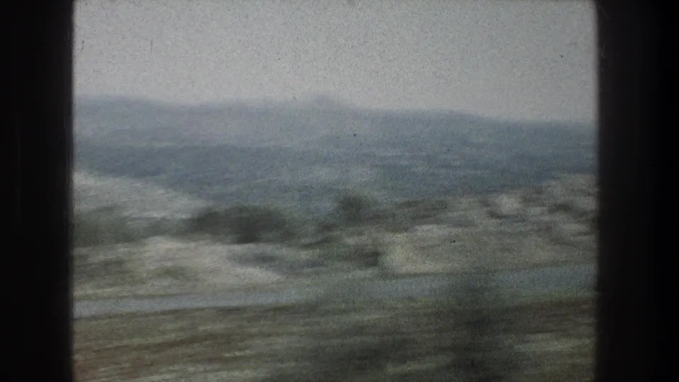 Late frame of the 1976 8mm Jerusalem-area window view, with hazy ridgelines, sparse brush, and motion-blurred foreground terrain.