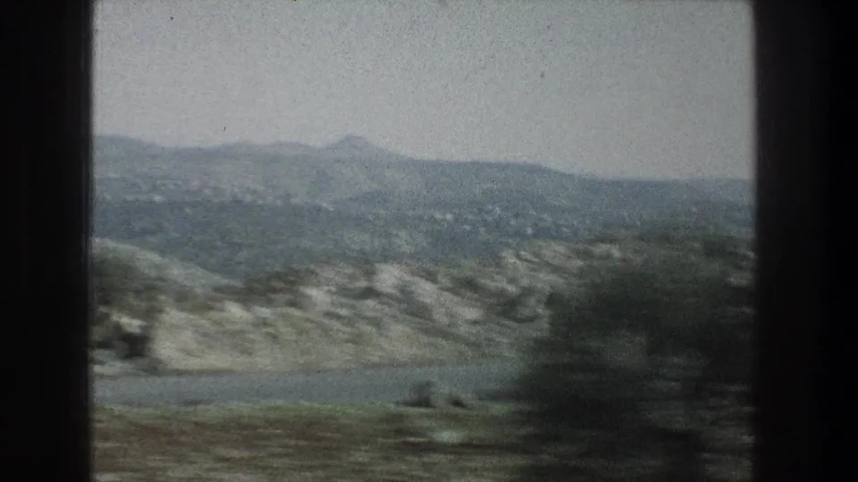 1976 8mm view of rocky terrain near Jerusalem, Israel, with distant hills under a hazy sky and dark frame borders.