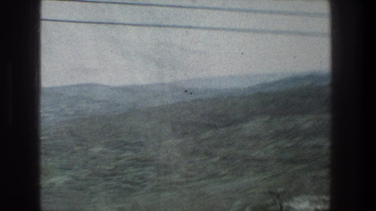 Rolling hills seen through dark vehicle window bars with utility wires crossing the sky.