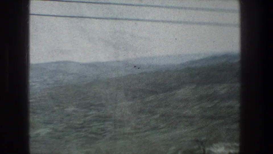 1976 8mm home-movie view near Jerusalem showing green hills and valleys through a moving vehicle window with overhead wires.