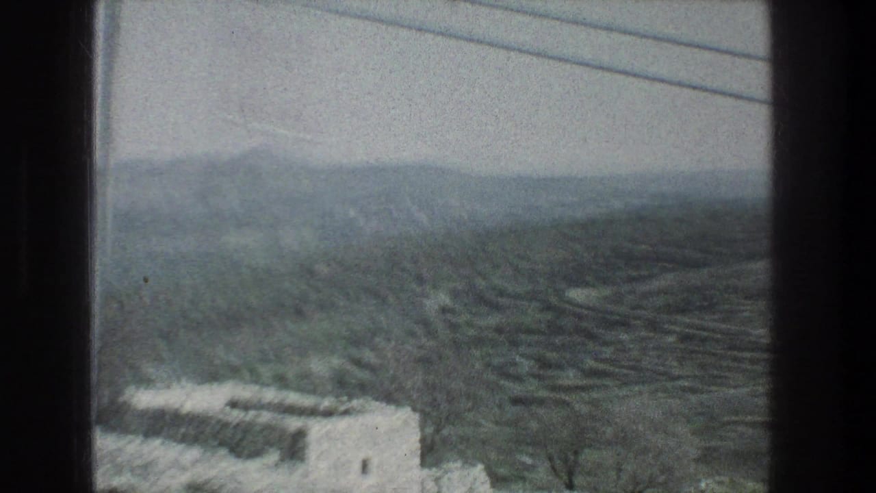 Moving-vehicle view near Jerusalem in 1976, with hills, valleys, utility lines, and a pale structure partly visible below the window frame.