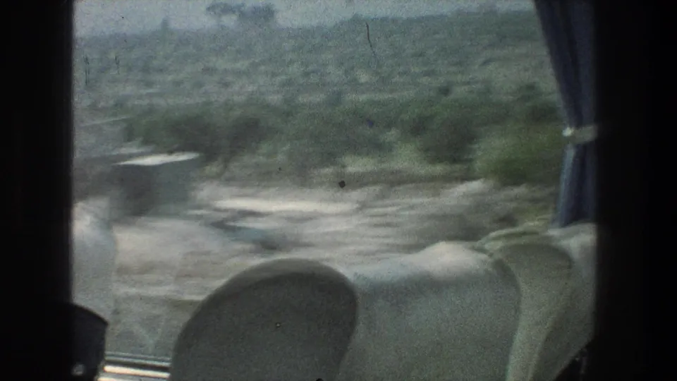 Interior passenger perspective from a moving vehicle near Jerusalem in 1976, showing roadside blur, hills, window framing, and part of a seat.